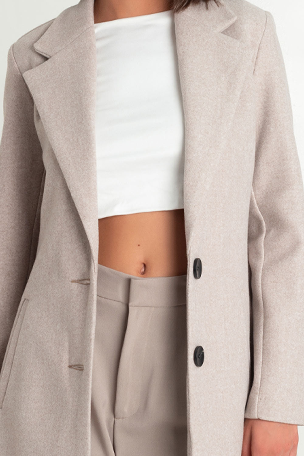 Abrigo largo de fit recto, con solapa y hombreras, manga larga, bolsillos delanteros con vivos y cierre frontal con botones en contraste.