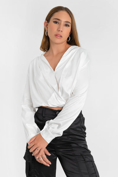 Blusa corta satinada de manga larga con puño abotonado, bajo elástico y escote v cruzado con detalles plisados en hombros.