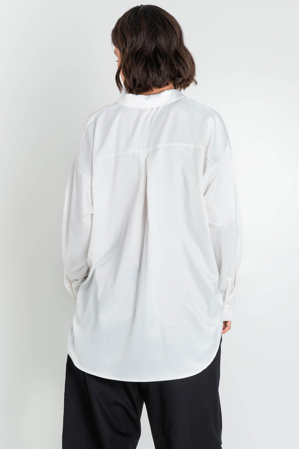 Camisa satinada de fit oversized, manga larga con puño abotonado, cuello camisero, bajo curveado, pinza de amplitud en espalda y cierre frontal con hilera de botones.