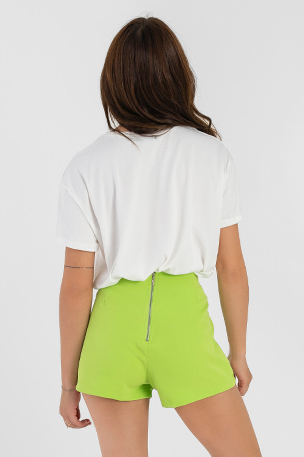 Falda short de fit ajustado, cintura alta, cruce frontal con bajo diagonal y cierre posterior con cremallera visible en contraste.