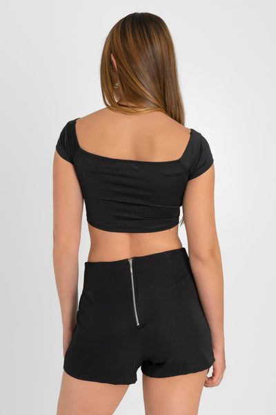 Falda short de fit ajustado, cintura alta, cruce frontal con bajo diagonal y cierre posterior con cremallera visible en contraste.