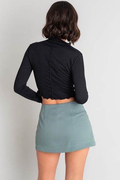 Falda short corto de cintura alta, corte en a, cruce frontal en diagonal con abertura y cierre lateral con cremallera oculta.