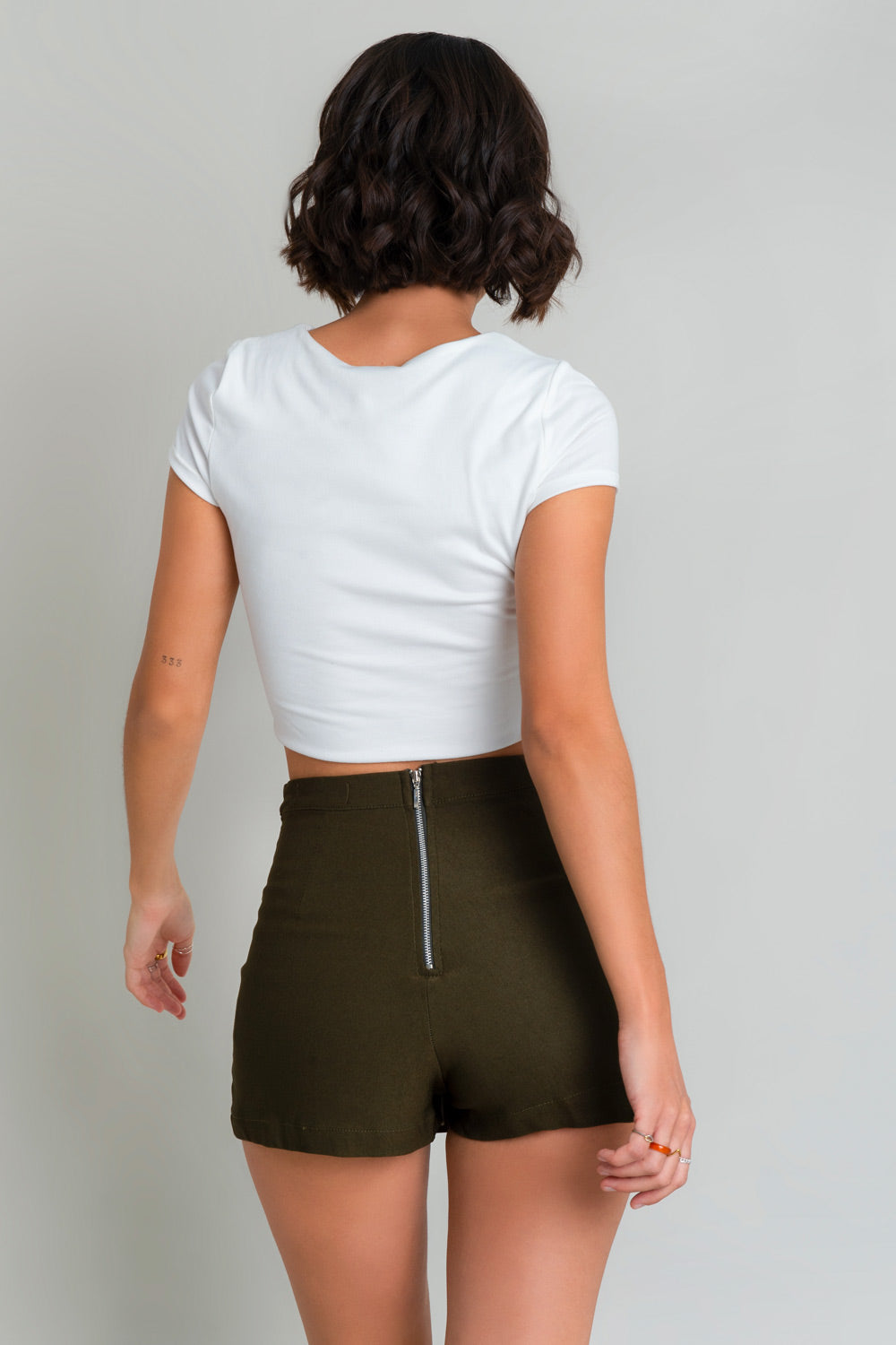 Falda short de fit ajustado, cintura alta con pretina, plisados frontales con abertura y cierre posterior con cremallera visible en contraste.