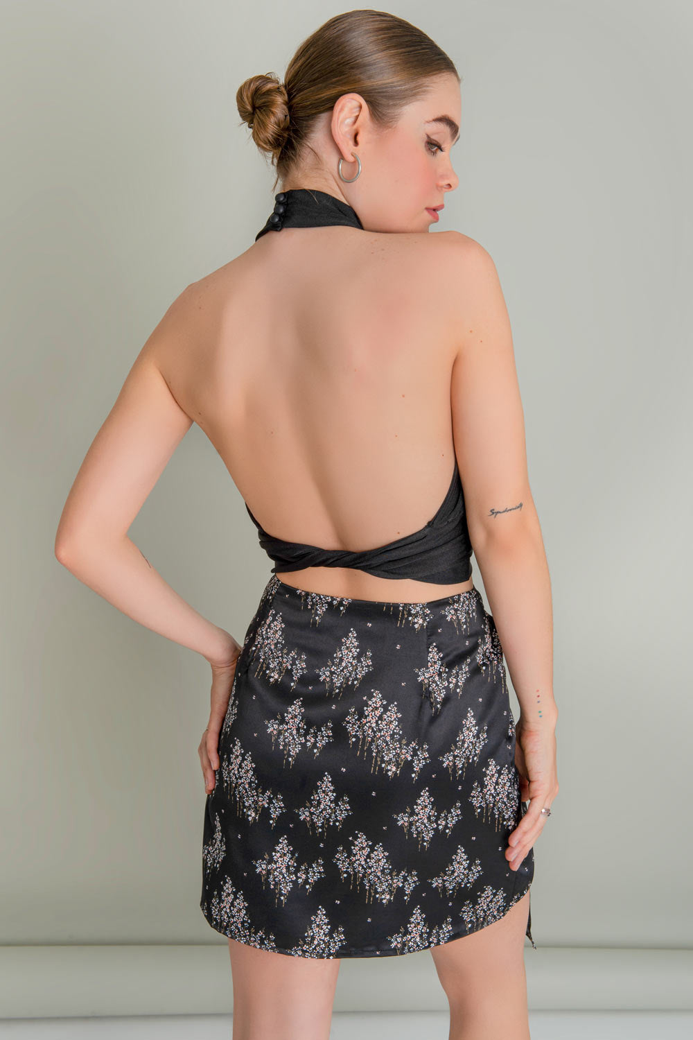 Falda corta satinada de estampado floral, corte en a, cintura alta, cruzado frontal con plisado lateral y nudo decorativo. Cierre lateral con cremallera oculta.