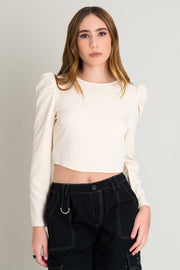 Blusa de cuello redondo, manga larga de hombro abullonado y escote en espalda. Cierre posterior con botón, ojal y lazo amarrable.
