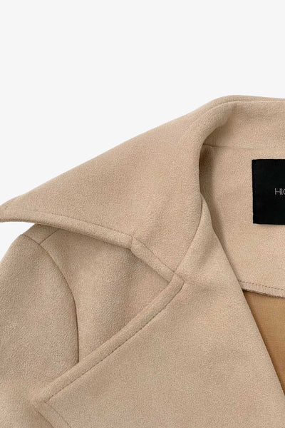 Abrigo abierto de gamuza, corte en a, con solapa y hombreras, manga larga, bolsillos delanteros ocultos, trabillas y cinturón amarrable del mismo tejido.