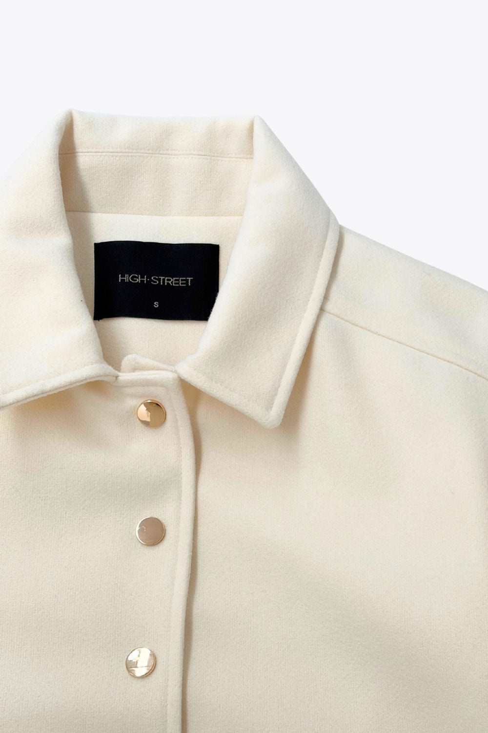 Abrigo corto de fit recto, manga larga, cuello solapa, bolsillos delanteros de parche con cartera y cierre frontal con hilera de botones en contraste.