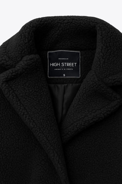 Abrigo largo de borreguillo, fit recto, con solapa, manga larga y bolsillos delanteros con vivos. Cierre frontal con botón en contraste.