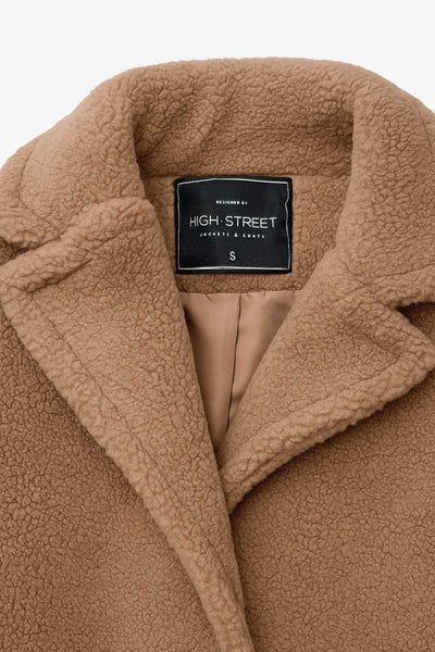 Abrigo largo de borreguillo, fit recto, con solapa, manga larga y bolsillos delanteros con vivos. Cierre frontal con botón en contraste.