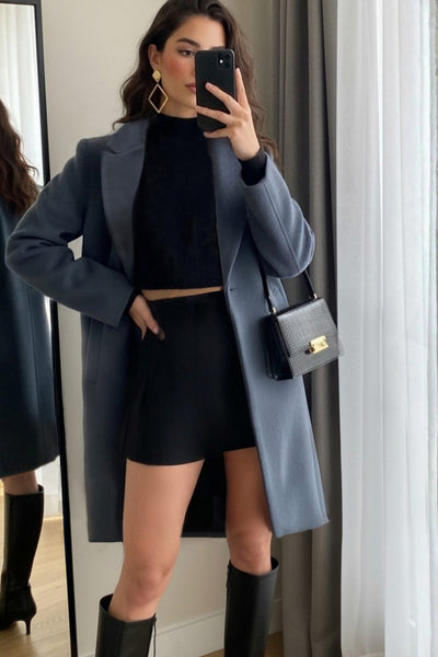 Abrigo largo de fit recto, con solapa, manga larga y bolsillos frontales con cartera. Cierre frontal con botón en contraste y detalle de abertura posterior.