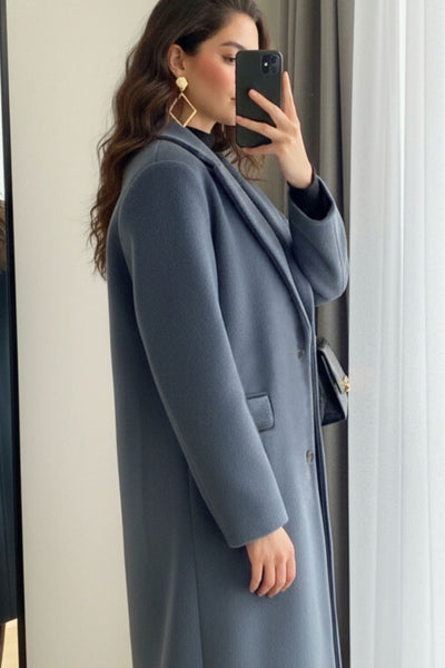 Abrigo largo de fit recto, con solapa, manga larga y bolsillos frontales con cartera. Cierre frontal con botón en contraste y detalle de abertura posterior.