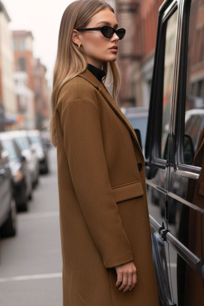 Abrigo largo de fit recto, con solapa, manga larga y bolsillos frontales con cartera. Cierre frontal con botón en contraste y detalle de abertura posterior.