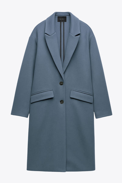 Abrigo largo de fit recto, con solapa, manga larga y bolsillos frontales con cartera. Cierre frontal con botón en contraste y detalle de abertura posterior.