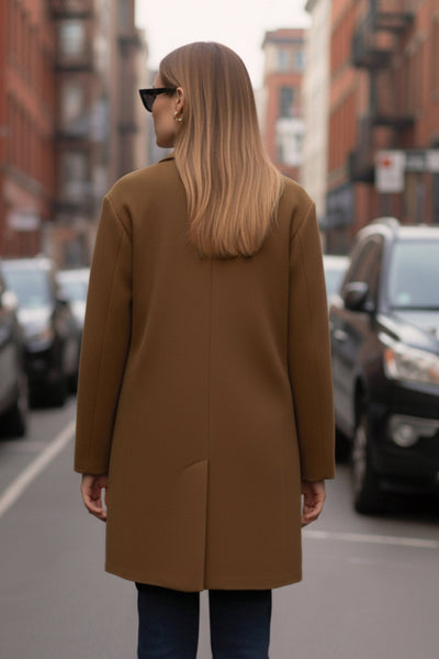 Abrigo largo de fit recto, con solapa, manga larga y bolsillos frontales con cartera. Cierre frontal con botón en contraste y detalle de abertura posterior.