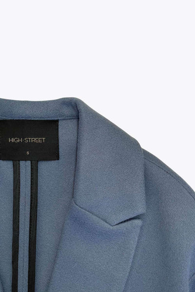 Abrigo largo de fit recto, con solapa, manga larga y bolsillos frontales con cartera. Cierre frontal con botón en contraste y detalle de abertura posterior.