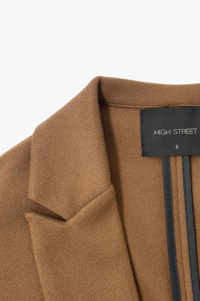 Abrigo largo de fit recto, con solapa, manga larga y bolsillos frontales con cartera. Cierre frontal con botón en contraste y detalle de abertura posterior.