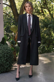 Abrigo largo de fit recto, manga larga, con solapa y hombreras, bolsillos delanteros con cartera y cierre frontal con cruce de botones. Detalle de abertura posterior en bajo.