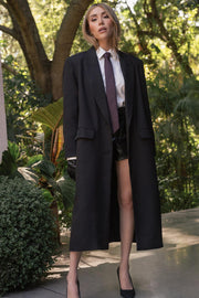 Abrigo largo de fit recto, manga larga, con solapa y hombreras, bolsillos delanteros con cartera y cierre frontal con cruce de botones. Detalle de abertura posterior en bajo.