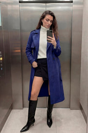 Abrigo trench midi de gamuza, fit recto, con solapa, bolsillos delanteros con vivos, detalle de bata frontal, manga larga con trabillas en puños y hombros, cinturón amarrable del mismo tejido y cierre frontal con doble cruce de botones en contraste.