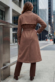 Abrigo trench midi de gamuza, fit recto, con solapa, bolsillos delanteros con vivos, detalle de bata frontal, manga larga con trabillas en puños y hombros, cinturón amarrable del mismo tejido y cierre frontal con doble cruce de botones en contraste.