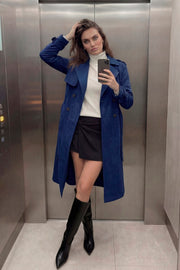 Abrigo trench midi de gamuza, fit recto, con solapa, bolsillos delanteros con vivos, detalle de bata frontal, manga larga con trabillas en puños y hombros, cinturón amarrable del mismo tejido y cierre frontal con doble cruce de botones en contraste.