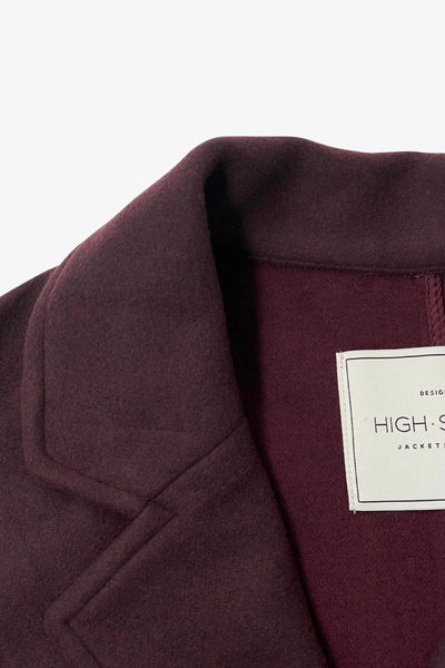 Abrigo largo de fit recto, manga larga, con solapa, bolsillos delanteros de parche y cierre frontal con cruce de botones en contraste.