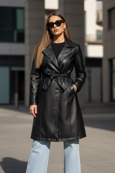 Abrigo trench de efecto piel, fit recto, con solapa, bolsillos delanteros con vivos, detalle de bata delantera y manga larga. Trabillas, cinturón amarrable del mismo tejido y cierre frontal con doble cruce de botón.