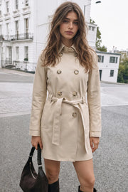 Abrigo trench corto de fit recto, con cuello solapa, bolsillos delanteros con vivos, detalle de bata trasera y manga larga. Trabillas, cinturón amarrable del mismo tejido y cierre frontal con doble cruce de botones en contraste. Detalle de trabilla y botón en hombros, bata trasera, cuello y puños.