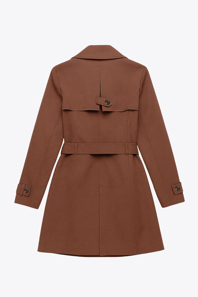 Abrigo trench corto de fit recto, con cuello solapa, bolsillos delanteros con vivos, detalle de bata trasera y manga larga. Trabillas, cinturón amarrable del mismo tejido y cierre frontal con doble cruce de botones en contraste. Detalle de trabilla y botón en hombros, bata trasera, cuello y puños.