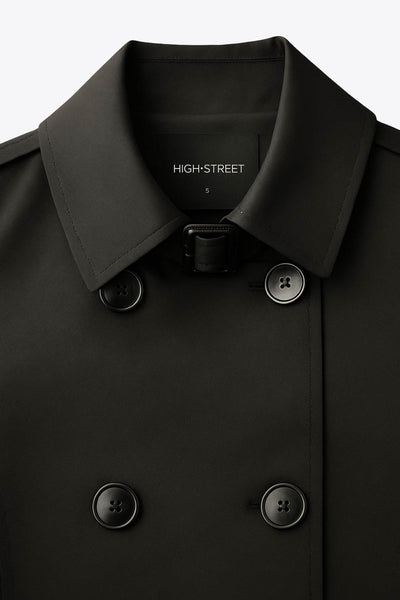 Abrigo trench corto de fit recto, con cuello solapa, bolsillos delanteros con vivos, detalle de bata trasera y manga larga. Trabillas, cinturón amarrable del mismo tejido y cierre frontal con doble cruce de botones en contraste. Detalle de trabilla y botón en hombros, bata trasera, cuello y puños.