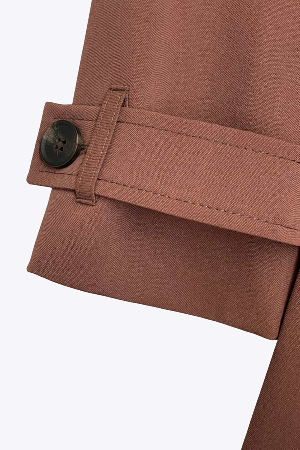 Abrigo trench corto de fit recto, con cuello solapa, bolsillos delanteros con vivos, detalle de bata trasera y manga larga. Trabillas, cinturón amarrable del mismo tejido y cierre frontal con doble cruce de botones en contraste. Detalle de trabilla y botón en hombros, bata trasera, cuello y puños.