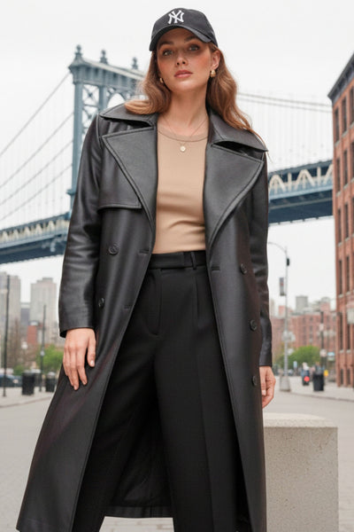 Abrigo trench largo de efecto piel, fit recto, manga larga, con solapa y bata en espalda, cortes decorativos frontales, trabillas y cinturón del mismo tejido con hebilla en contraste. Cierre frontal con doble cruce de botones en contraste.