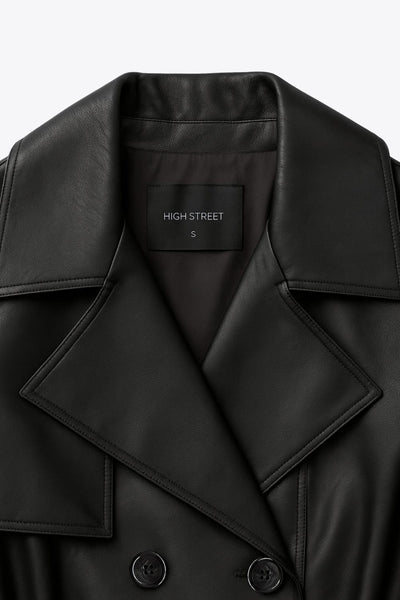 Abrigo trench largo de efecto piel, fit recto, manga larga, con solapa y bata en espalda, cortes decorativos frontales, trabillas y cinturón del mismo tejido con hebilla en contraste. Cierre frontal con doble cruce de botones en contraste.