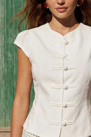 Blusa corta de fit ajustado, cuello mao, manga corta con plisados en hombros, cierre frontal con botones y detalle de lazo amarrable posterior.