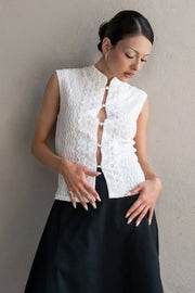 Blusa de fit ajustado, sin mangas, cuello mao, cut out frontal con hilera de botones y detalle de textura en tejido. Detalle de encaje decorativo.
