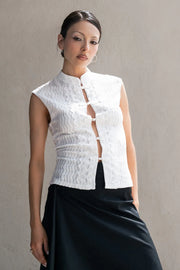 Blusa de fit ajustado, sin mangas, cuello mao, cut out frontal con hilera de botones y detalle de textura en tejido. Detalle de encaje decorativo.
