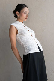 Blusa de fit ajustado, sin mangas, cuello mao, cut out frontal con hilera de botones y detalle de textura en tejido. Detalle de encaje decorativo.
