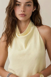 Blusa corta de lino, fit fluido, sin mangas, cuello halter fluido con plisados, escote en espalda y lazo amarrable posterior. Cierre posterior con botón y ojal.