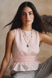 Blusa corta de cuello barco, sin mangas, rib con plisados en cintura, peplum con olanes en bajo y detalle de jaretas ajustables en costados. Cierre posterior con botón y ojal.