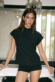 Blusa de cuello alto fluido, plisados en hombros, manga corta seguida y fit recto. Cierre posterior con botón y ojal.