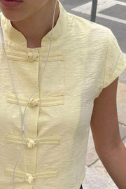 Blusa corta de fit recto, cuello mao, manga corta y cierre frontal con botones alamares.
