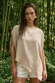 Blusa tipo capa de fit fluido, manga corta seguida, cuello barco y bajo asimétrico diagonal. Cierre posterior con cremallera oculta.