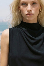 Blusa sin mangas de fit recto, cuello mock con detalles plisados y cierre posterior con botón y ojal.