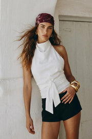 Blusa de fit recto, halter con cuello fluido, sin mangas, lazo amarrable en cintura, cierre posterior con botón y ojal.