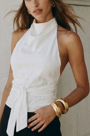 Blusa de fit recto, halter con cuello fluido, sin mangas, lazo amarrable en cintura, cierre posterior con botón y ojal.