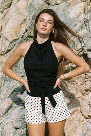 Blusa de fit recto, halter con cuello fluido, sin mangas, lazo amarrable en cintura, cierre posterior con botón y ojal.