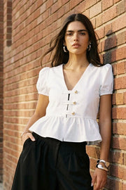 Blusa corta de fit recto, manga corta abullonada con rib elástico en bordes, escote v, peplum con olanes y cierre frontal con hilera de botones en contraste.