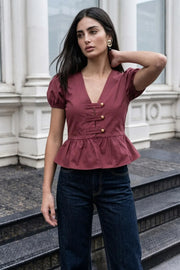Blusa corta de fit recto, manga corta abullonada con rib elástico en bordes, escote v, peplum con olanes y cierre frontal con hilera de botones en contraste.