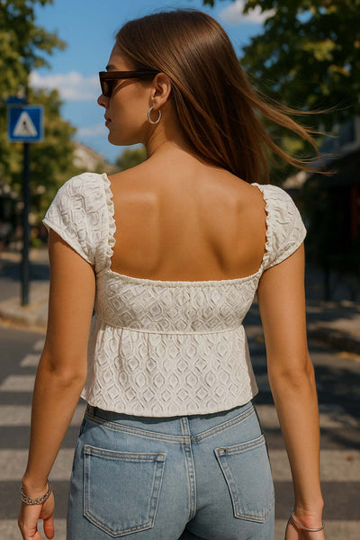 Blusa corta de escote v con cortes, olanes en borde y lazo decorativo frontal, manga corta y peplum con olanes en bajo. Detalle de textura en tejido.