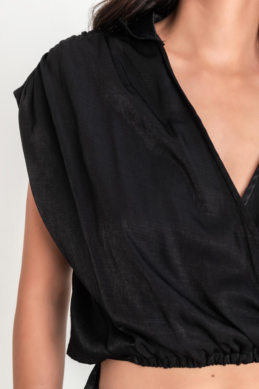 Blusa corta plisada sin mangas, de escote v cruzado con plisados en hombros, cuello camisero, pinza de amplitud en espalda y plisado en bajo con lazo amarrable en cintura.